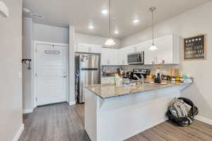 Kitchen with appliances with stainless steel finishes, kitchen peninsula, pendant lighting, and white cabinets