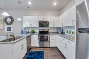 Kitchen with appliances with stainless steel finishes, white cabinetry, sink, and decorative light fixtures