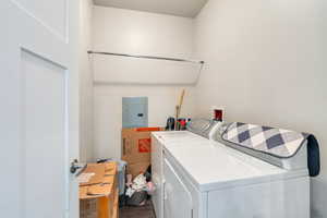 Washroom with hardwood / wood-style floors, electric panel, and washing machine and clothes dryer