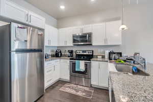 Kitchen featuring sink, white cabinets, stainless steel appliances, decorative light fixtures, and dark hardwood / wood-style flooring