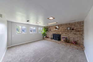 Unfurnished living room with baseboards, a brick fireplace, carpet, and visible vents