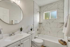 Full bathroom with tiled shower / bath combo, vanity, and toilet