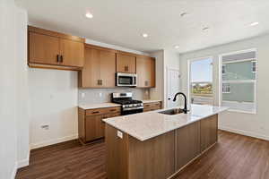 Kitchen featuring sink, dark wood-type flooring, decorative backsplash, a center island with sink, and appliances with stainless steel finishes