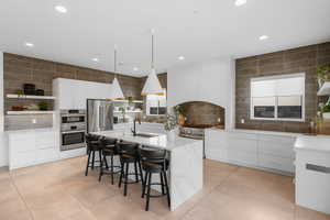 Kitchen with decorative light fixtures, high quality appliances, an island with sink, white cabinets, and light tile patterned floors