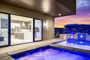 Pool at dusk featuring an in ground hot tub and an outdoor wet bar