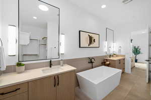 Bathroom with tile patterned flooring, vanity, a bath, and tile walls