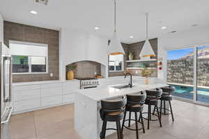 Kitchen with sink, high end appliances, an island with sink, white cabinets, and decorative backsplash