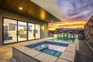 Pool at dusk with an in ground hot tub and a patio