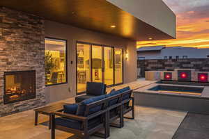 Patio terrace at dusk featuring an in ground hot tub and an outdoor living space with a fireplace