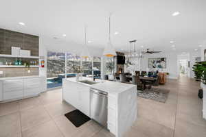 Kitchen featuring sink, decorative light fixtures, stainless steel dishwasher, an island with sink, and white cabinets