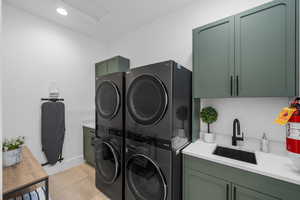 Laundry room featuring cabinets, sink, and stacked washer and dryer