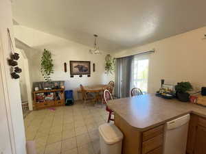 Kitchen with hanging light fixtures, vaulted ceiling, a chandelier, white dishwasher, and light tile patterned floors