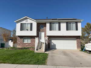 Split foyer home with a garage, a front lawn, and solar panels