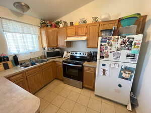 Kitchen with light tile patterned floors, sink, a textured ceiling, stainless steel appliances, and vaulted ceiling