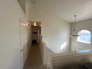 Corridor featuring light carpet, a textured ceiling, and high vaulted ceiling