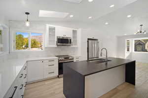 Kitchen featuring lofted ceiling with skylight, sink, hanging light fixtures, appliances with stainless steel finishes, and an island with sink