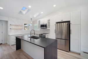 Kitchen with white cabinetry, sink, stainless steel appliances, and vaulted ceiling with skylight