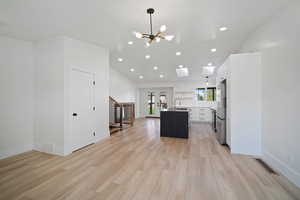 Kitchen featuring a skylight, a kitchen island with sink, light wood-type flooring, decorative light fixtures, and white cabinetry