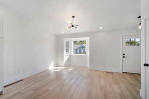 Unfurnished living room with an inviting chandelier, light hardwood / wood-style flooring, and plenty of natural light