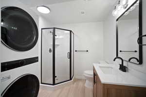 Bathroom with vanity, stacked washer / drying machine, hardwood / wood-style floors, an enclosed shower, and toilet