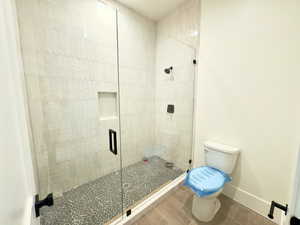 Bathroom featuring wood-type flooring, a shower with door, and toilet