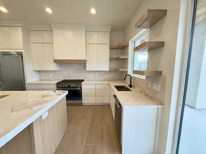 Kitchen with stainless steel appliances, light stone countertops, white cabinets, and sink