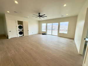 Unfurnished living room featuring stacked washer / dryer, light hardwood / wood-style flooring, and ceiling fan