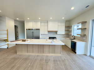 Kitchen featuring light wood-type flooring, a center island with sink, sink, stainless steel appliances, and white cabinets