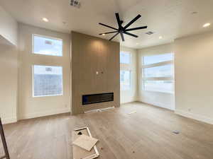 Unfurnished living room with a fireplace, light wood-type flooring, and ceiling fan