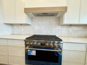 Kitchen featuring light stone counters, decorative backsplash, high end stainless steel range, and exhaust hood