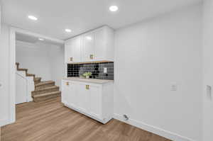 Laundry with decorative backsplash, white cabinets, and light hardwood / wood-style flooring