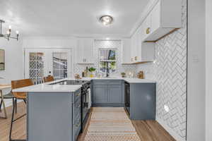 Kitchen with pendant lighting, kitchen peninsula, gray cabinetry, black appliances, and light hardwood / wood-style floors