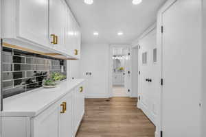 Interior space with white cabinets, light wood-type flooring, backsplash, and light stone countertops