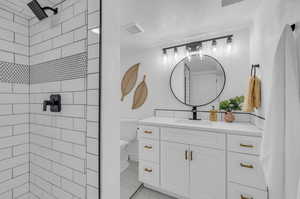 Bathroom featuring a textured ceiling, a tile shower, vanity, and toilet