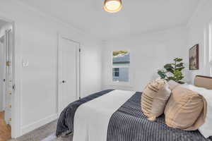 Bedroom with ornamental molding and light colored carpet