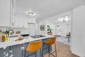 Kitchen with light wood-type flooring, black stovetop, decorative backsplash, white cabinets, and a breakfast bar area