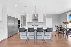 Kitchen with wood-type flooring, wall chimney range hood, hanging light fixtures, and stainless steel appliances