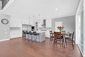 Kitchen featuring wall chimney exhaust hood, a kitchen island with sink, dark hardwood / wood-style floors, high end fridge, and hanging light fixtures