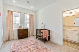 Bedroom with a crib, ensuite bathroom, sink, and light colored carpet