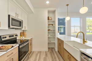 Kitchen featuring sink, decorative light fixtures, white cabinets, light brown cabinets, and appliances with stainless steel finishes