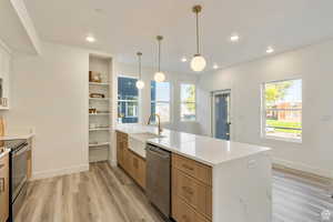 Kitchen featuring stainless steel appliances, sink, light stone counters, light brown cabinets, and hanging light fixtures