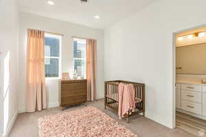 Bedroom featuring a nursery area, light colored carpet, and connected bathroom