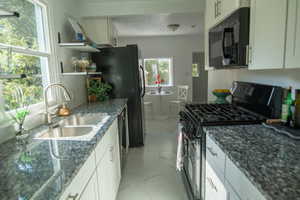 Kitchen featuring white cabinets, sink, a textured ceiling, black appliances, and dark granite counters