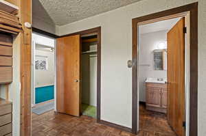 Unfurnished bedroom with dark parquet floors, a closet, sink, connected bathroom, and a textured ceiling