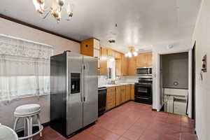 Kitchen with ceiling fan with notable chandelier, crown molding, dark tile patterned flooring, sink, and black appliances