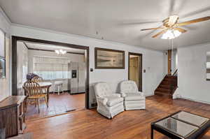 Living room featuring ceiling fan with notable chandelier, hardwood / wood-style flooring, and crown molding