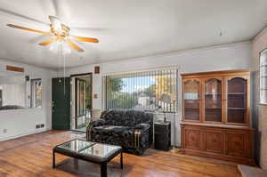 Living room featuring wood-type flooring, crown molding, and ceiling fan