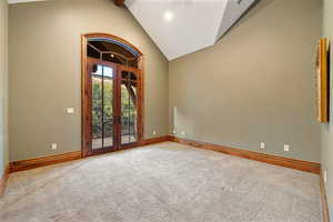 Carpeted spare room featuring french doors and high vaulted ceiling