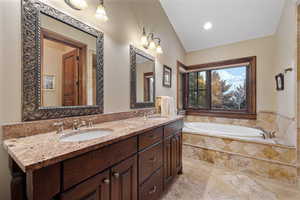 Bathroom with lofted ceiling, a relaxing tiled tub, and vanity