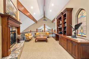 Library, Living room featuring light carpet, lofted ceiling with beams, a premium fireplace, and ceiling fan